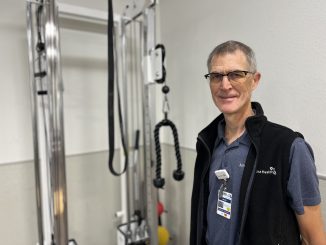 David Pierson stand in front of medical equipment and smiles at the camera